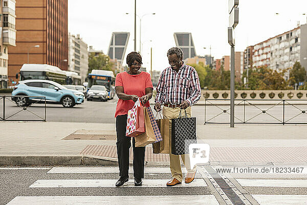Happy couple with shopping bags crossing road in city