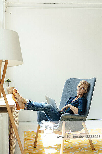Businesswoman with laptop on armchair at workplace