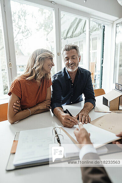 Glücklicher Mann und Frau unterzeichnen Vertrag mit Immobilienmakler