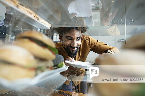 Smiling cafe owner removing burger from display cabinet at coffee shop