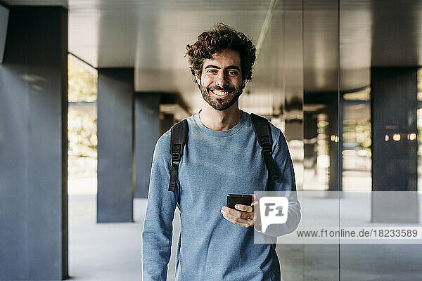 Happy man with smart phone standing in corridor