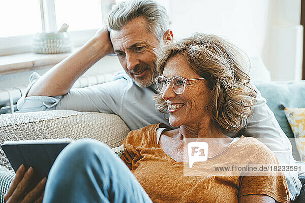 Happy mature woman wearing eyeglasses using tablet PC by man at home