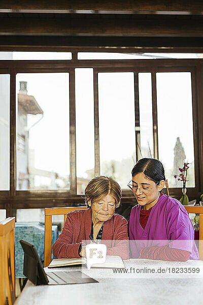 Healthcare worker with senior woman writing in diary at table