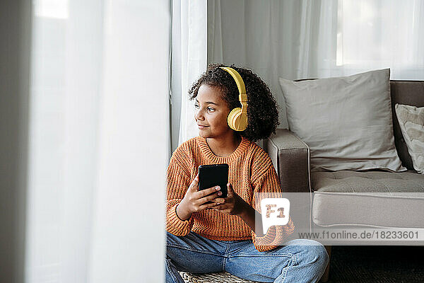 Smiling girl wearing wireless headphones sitting with smart phone at home