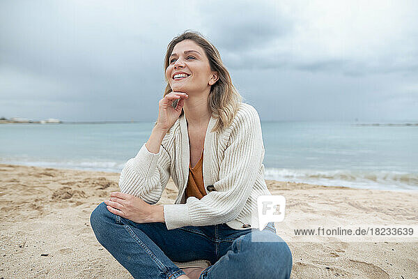Smiling young beautiful woman sitting on sand day dreaming at beach