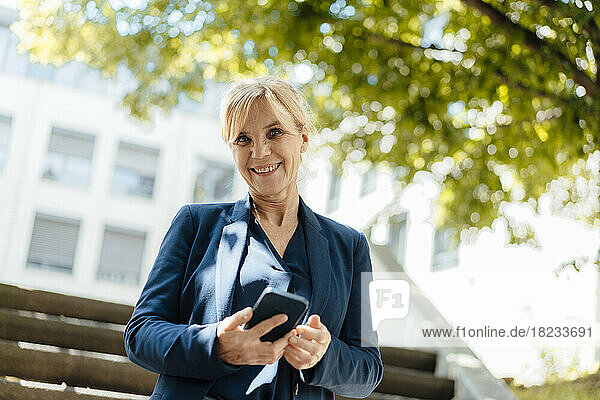 Happy businesswoman with smart phone on sunny day