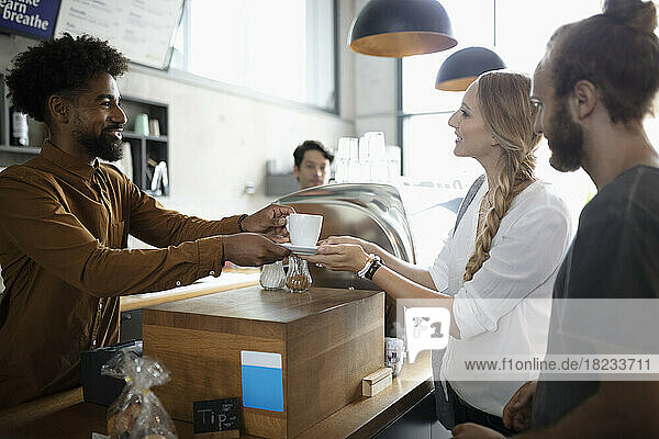 Smiling barista serving coffee to couple in cafe