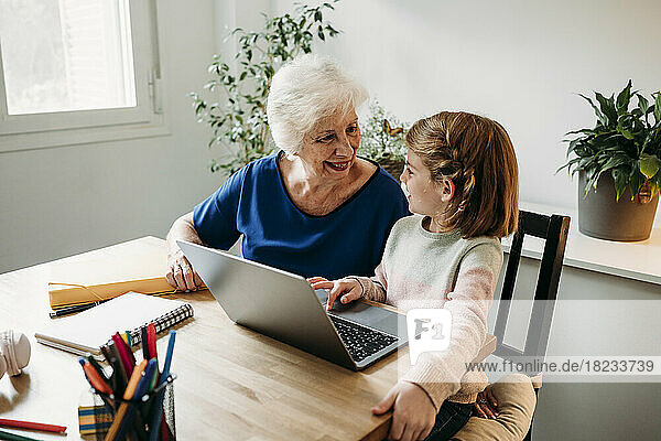 Glückliches Mädchen mit Laptop auf dem Tisch und Blick auf die Großmutter