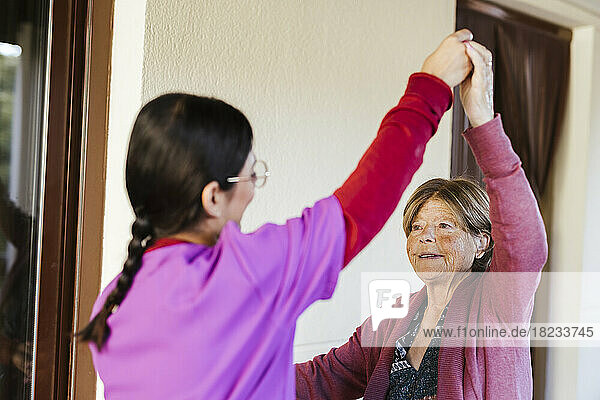 Young caregiver helping senior woman to exercise at home