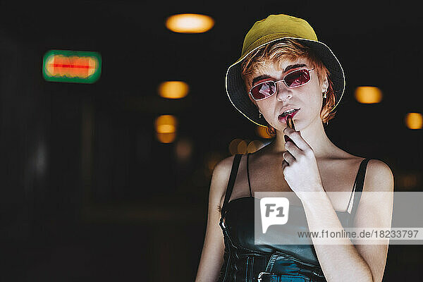 Young woman wearing sunglasses applying lipstick in underpass