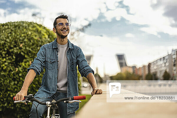 Happy young man sitting on bicycle under cloudy sky