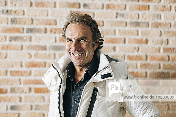 Happy mature man wearing jacket in front of brick wall