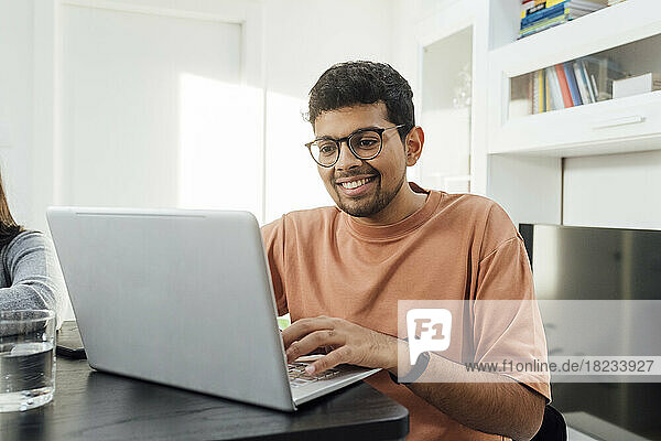Glücklicher Mann lernt mit Laptop auf dem Tisch im Wohnzimmer