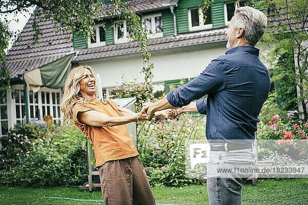 Cheerful mature woman holding hands with man and having fun in front of house