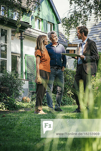 Mature couple discussing with real estate agent in backyard