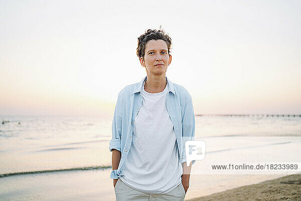 Androgynous woman standing with hands in pockets at beach
