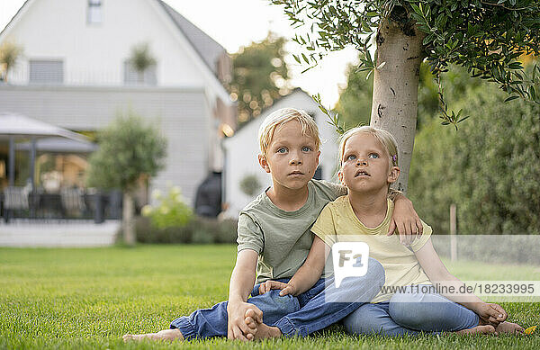 Junge sitzt mit Arm um Schwester auf Gras im Hinterhof
