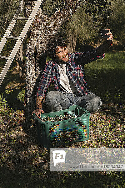 Glücklicher Mann mit Olivenkiste  der ein Selfie mit dem Handy macht