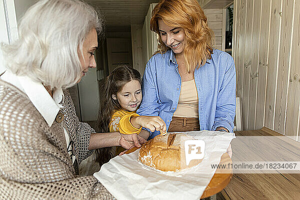 Grandmother  mother and granddaughter holding freshly baked homemade bread in kitchen