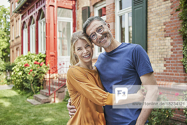 Smiling woman embracing man in front of house at back yard