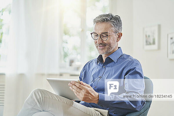 Lächelnder Geschäftsmann nutzt Tablet-PC im Sessel zu Hause