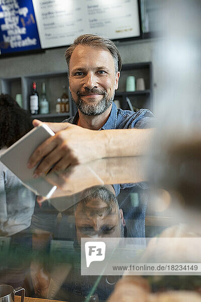 Smiling cafe owner with tablet PC standing at counter in coffee shop