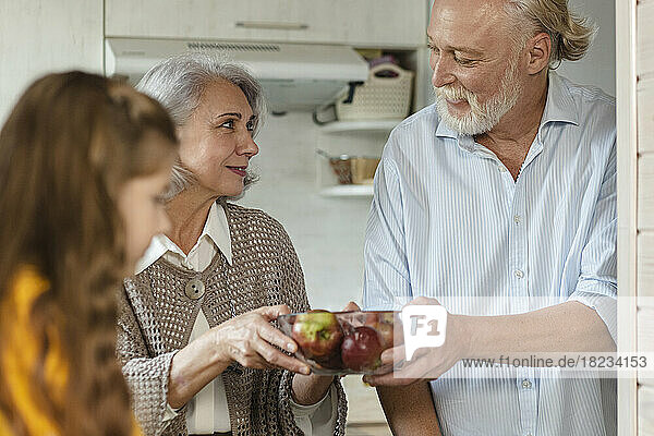 Grandparents holding bowl of fresh apples in kitchen