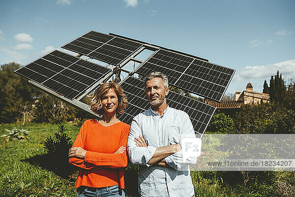 Smiling mature couple in front of solar panels on sunny day