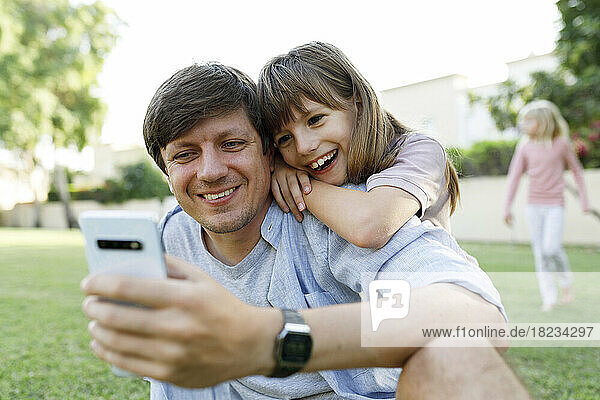 Happy daughter with father using smart phone in park