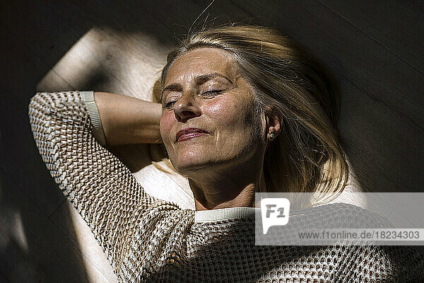 Mature woman with hands behind head relaxing on floor at home