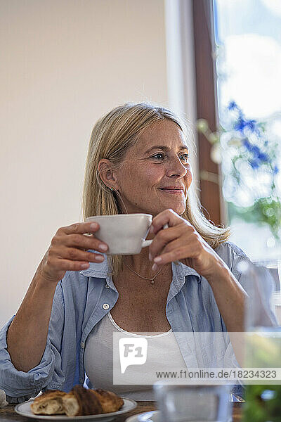 Lächelnde reife Frau hält zu Hause eine Tasse Kaffee