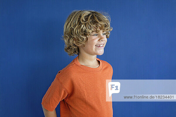 Smiling boy wearing orange t-shirt against blue background