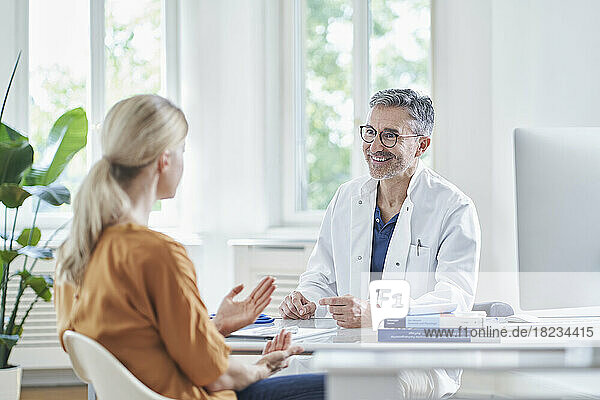Happy doctor with patient sitting at desk in medical practice