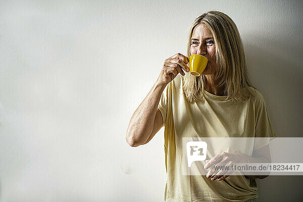 Reife Frau trinkt Kaffee vor der Wand