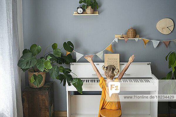 Mädchen mit erhobenen Händen sitzt zu Hause am Klavier