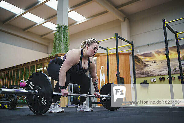 Confident overweight woman exercising with barbell in gym