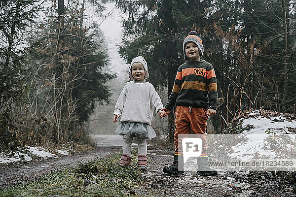 Happy siblings holding hands standing in forest