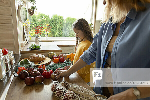Mother and daughter unpacking fresh groceries in kitchen