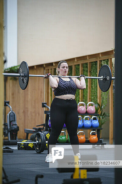 Determined young woman lifting barbell in gym