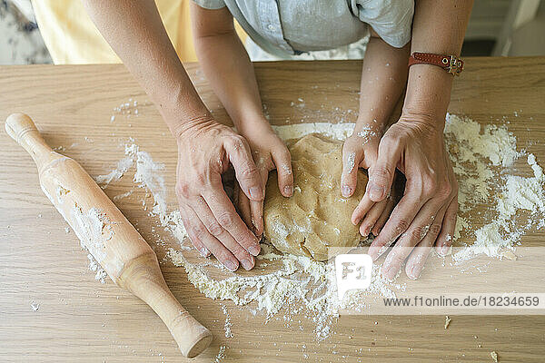 Hands of woman kneading cookie dough on table at home