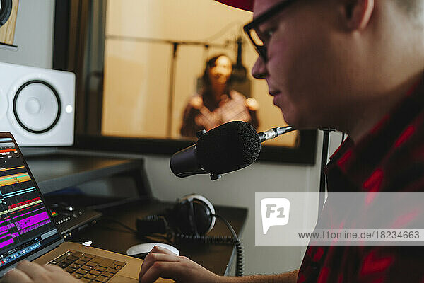 Toningenieur komponiert am Laptop mit Sänger im Hintergrund im Aufnahmestudio