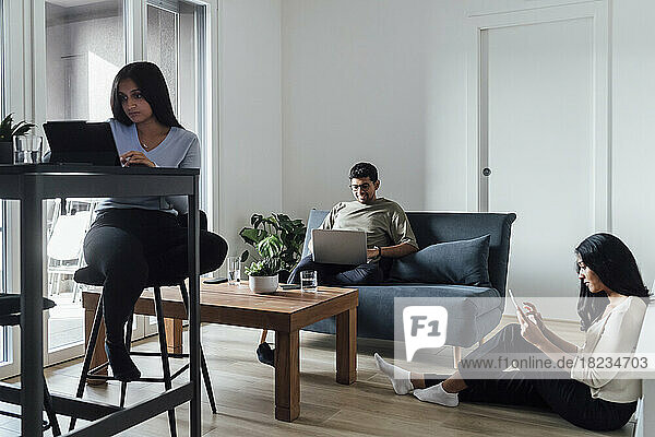 Zwei Frauen und ein Mann lernen mithilfe drahtloser Technologien im Wohnzimmer