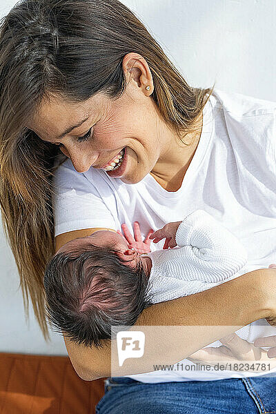 Happy mother playing with newborn daughter at home