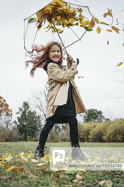 Fröhliches Mädchen  das Spaß mit Regenschirm im Park hat