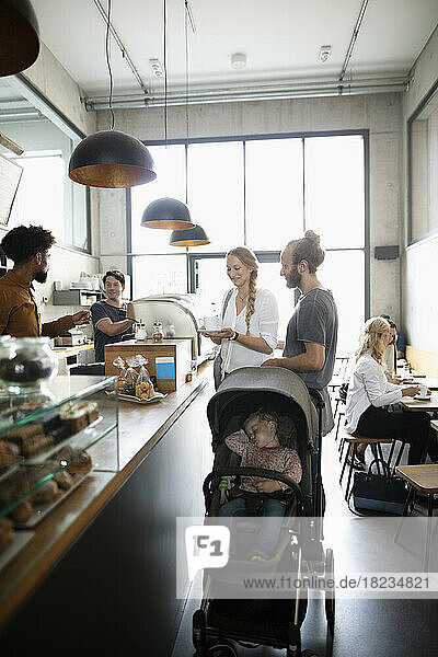 Smiling parents with daughter in stroller ordering at coffee shop