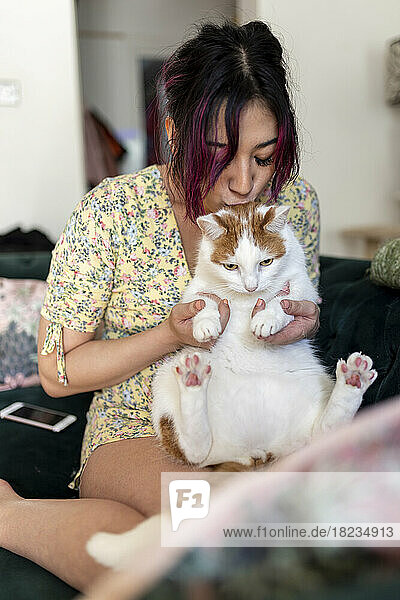 Young woman kissing and playing with cat at home