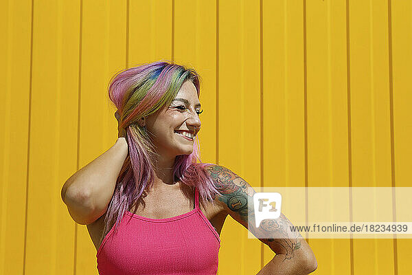 Happy woman with colorful dyed hair in front of yellow wall