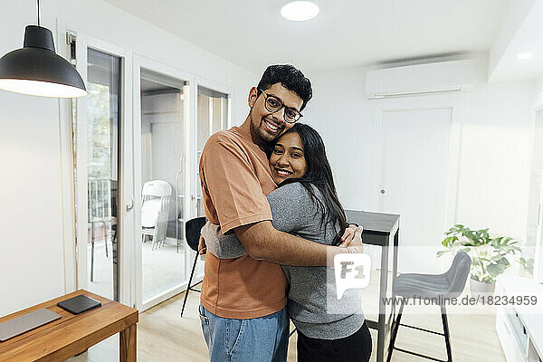 Lächelnder Mann umarmt glückliche Frau im heimischen Wohnzimmer