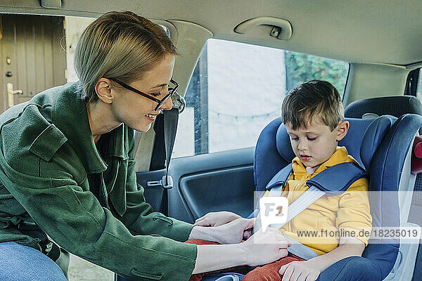 Happy mother fastening seat belt over son sitting in car
