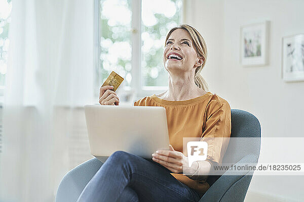 Happy woman with credit card enjoying online shopping through laptop at home